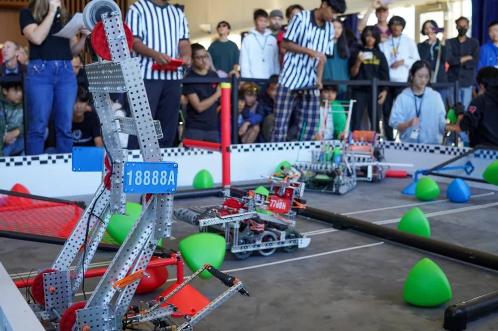 Two competition robots on the One World field with referees and the crowd behind