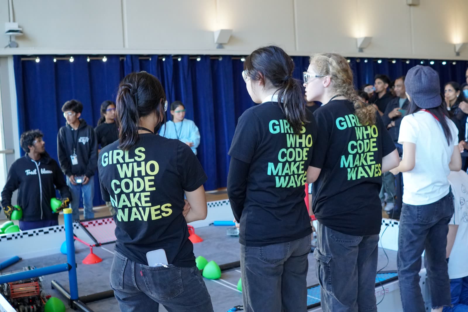 Team members in Girls Who Code Make Waves shirts watching a match at the field