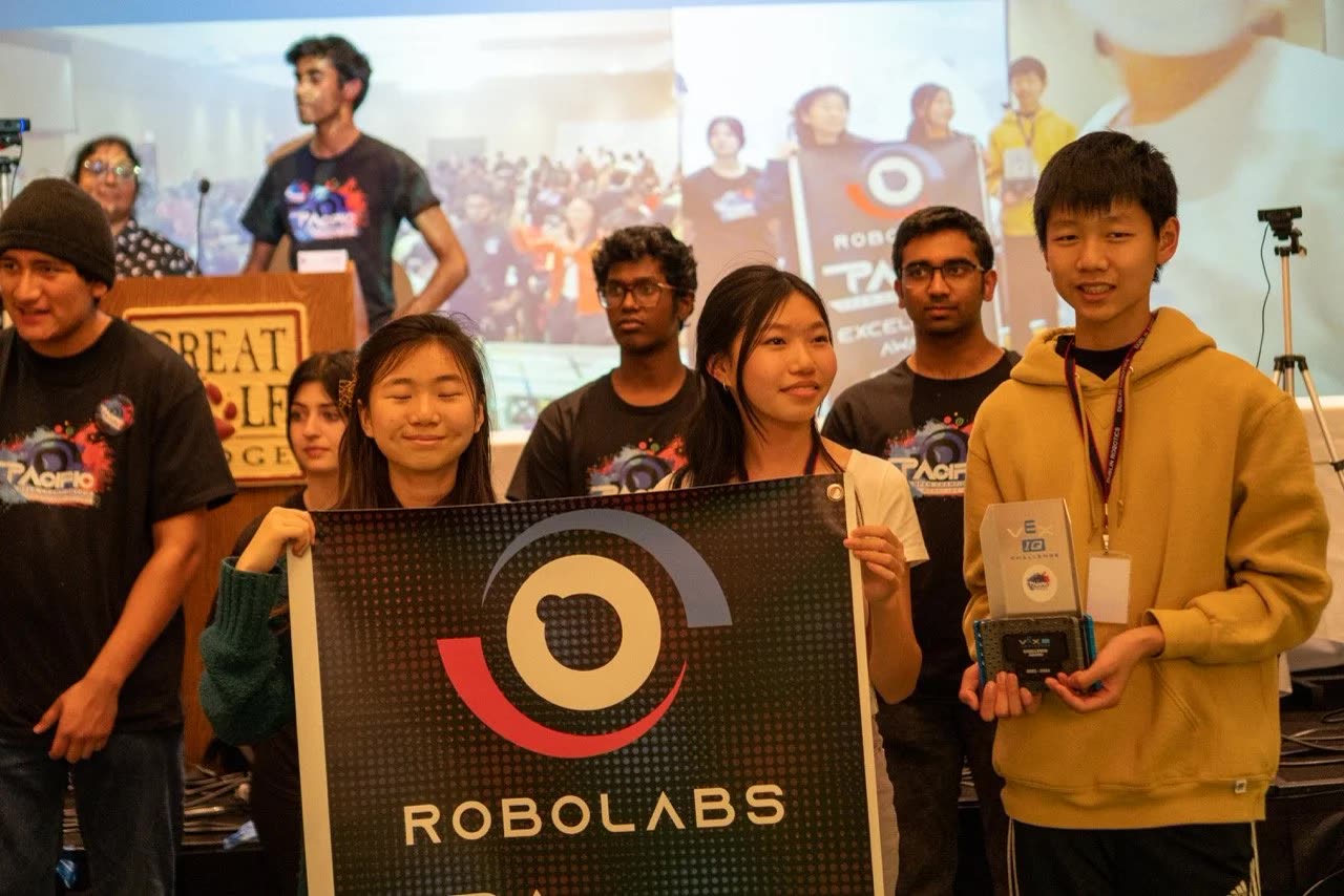 A winning team on stage with their trophies and the Robolabs banner at the Pacific Open Championship
