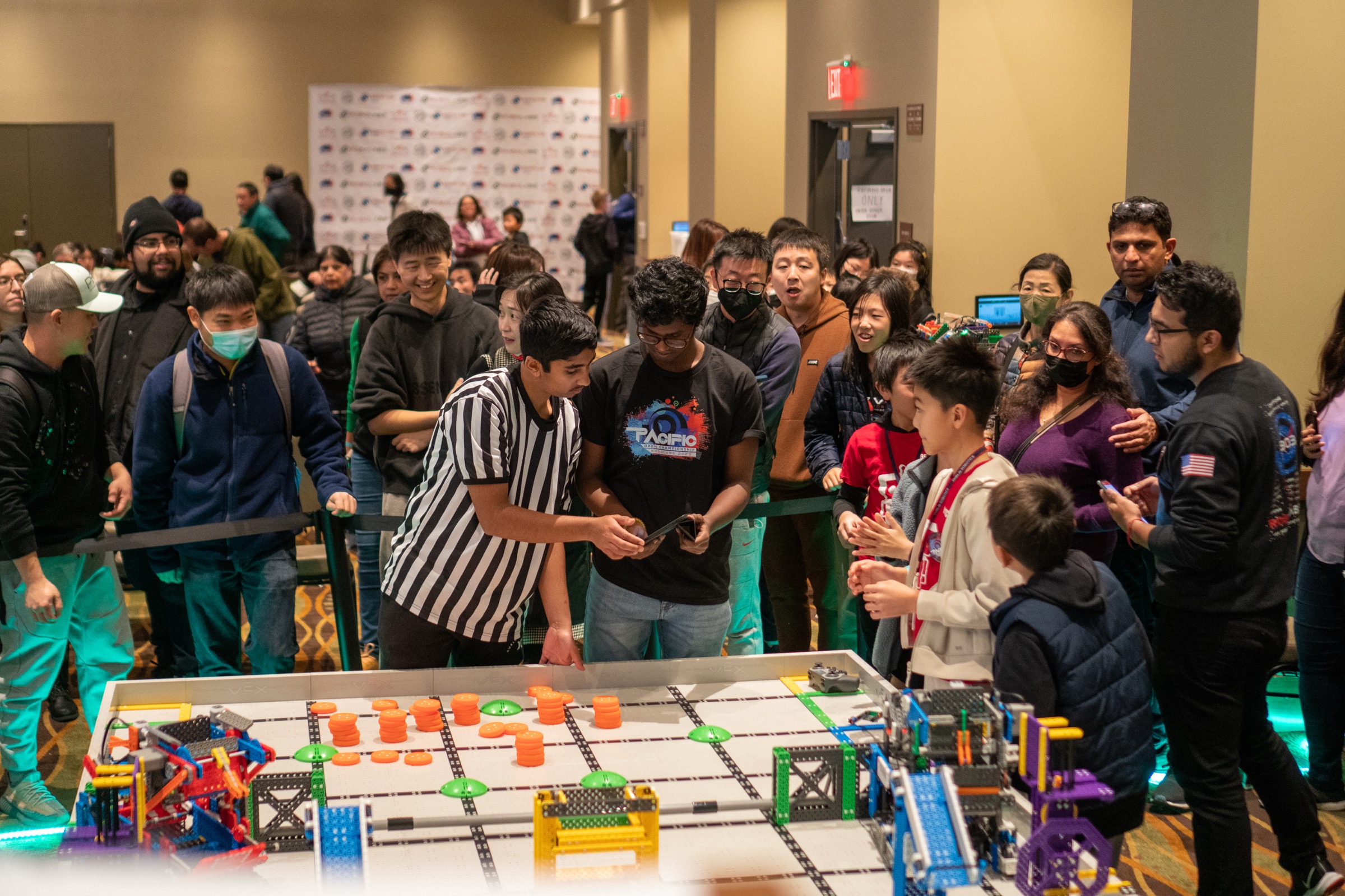 A crowd three deep around a competition field at the Robolabs Pacific Open Championship in 2023, the referee in the event tee running the match