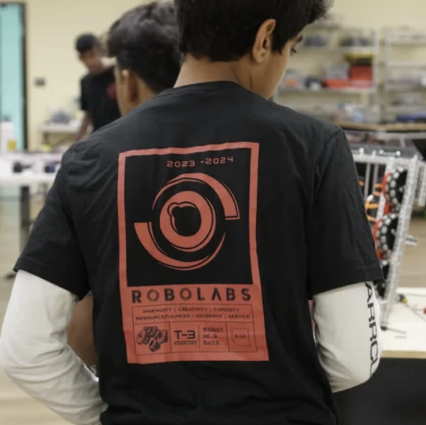 A student in a Robolabs Ri3D shirt reading Robot in 3 Days working on a competition robot